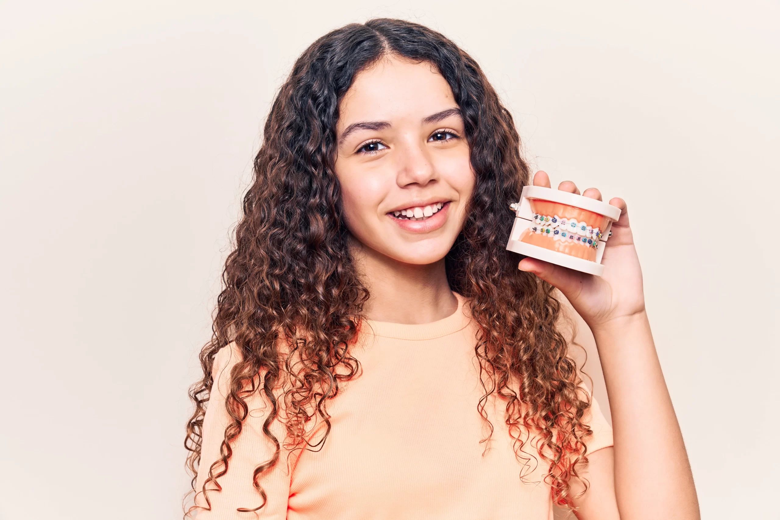 Smiling girl holding dental braces model