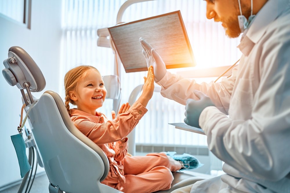 a,little,girl,is,sitting,in,a,dentist's,chair,,giving