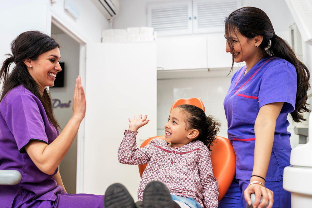 Dentists greeting child in clinic with high five.