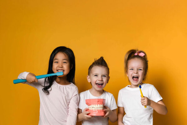Three children brushing teeth happily with large toothbrush.