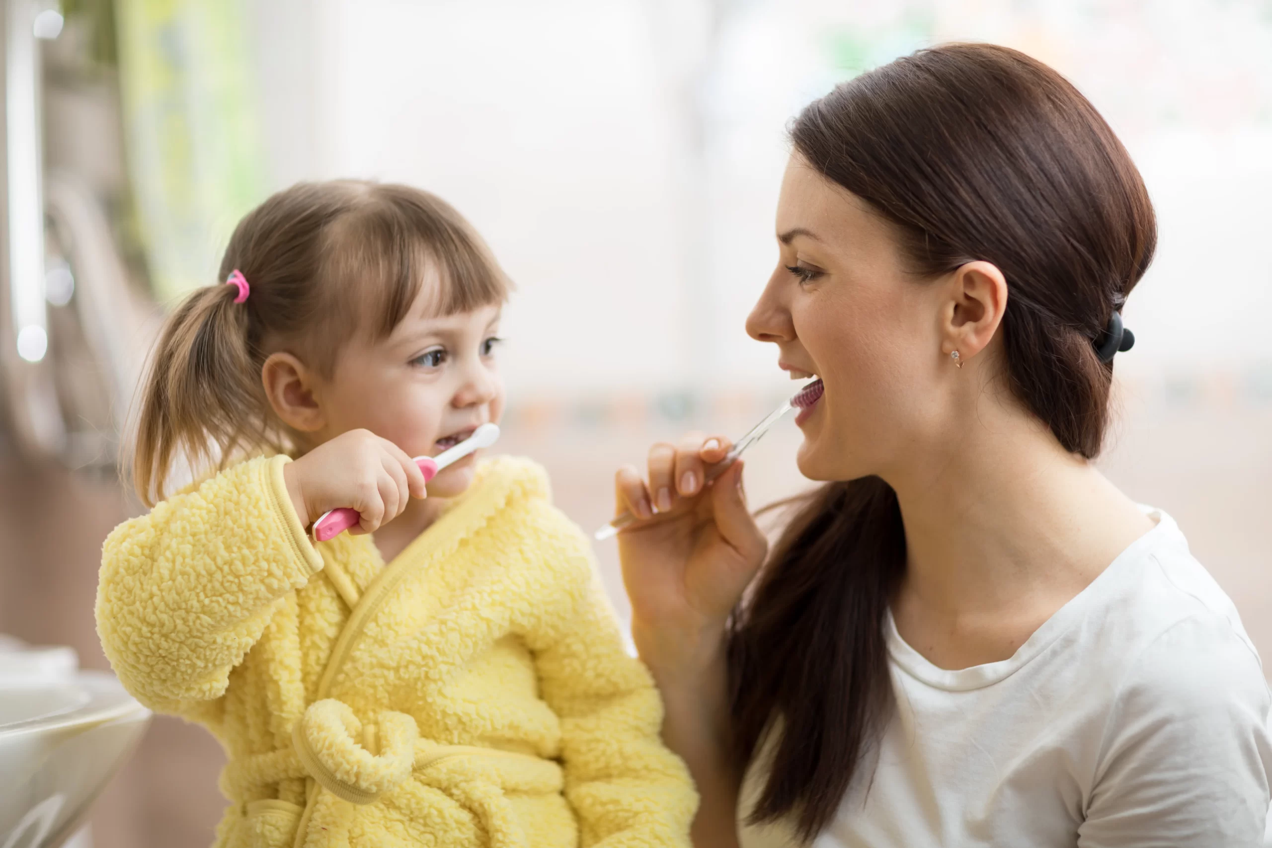 Mother and daughter brushing teeth together, smiling.