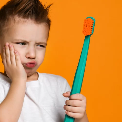 Child with toothache holding toothbrush, orange background.