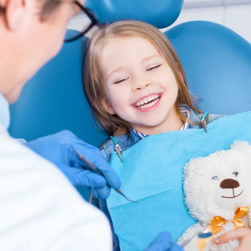 Child smiling at dentist holding teddy bear during dental sealant for kids appointment