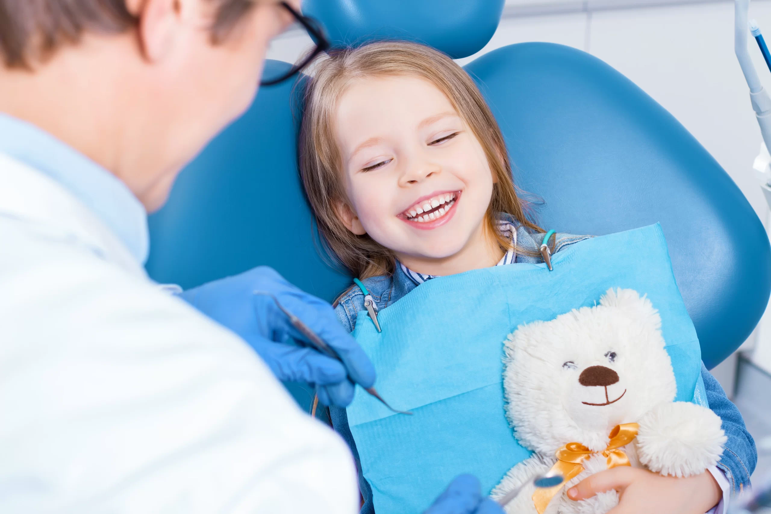 Child smiling at dentist holding teddy bear during dental sealant for kids appointment