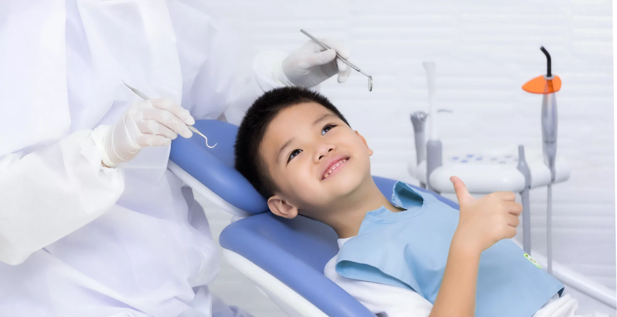 Smiling child at dentist giving thumbs up.