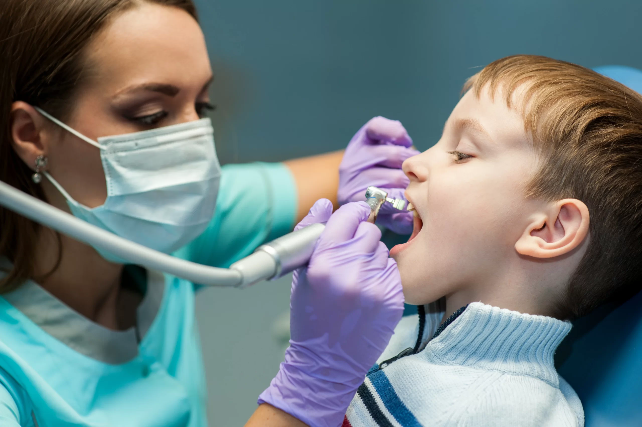 Dentist examines child's teeth with dental tools.