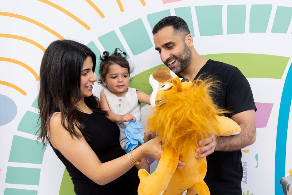 Family smiling with child holding lion toy.