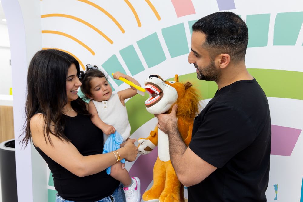 Child brushing lion puppet's teeth with parents watching.