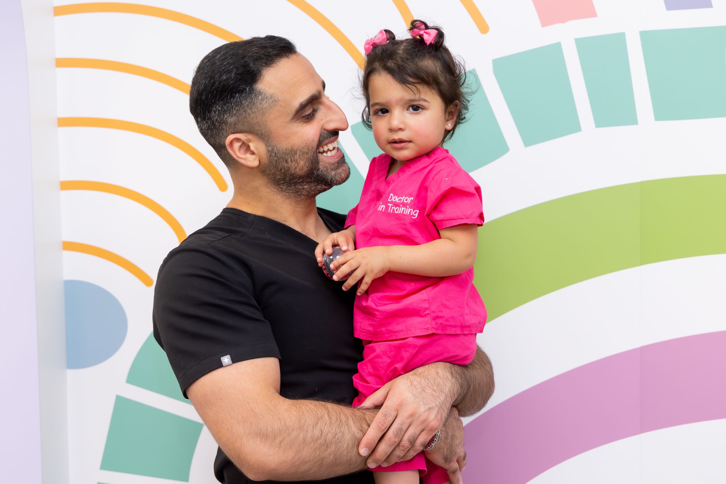 Smiling man holds child in pink outfit.