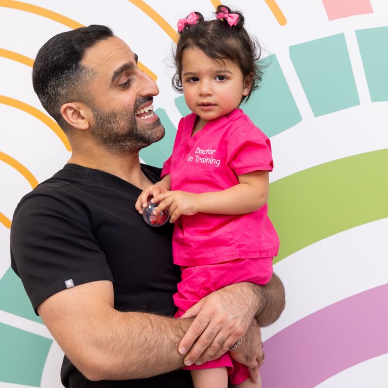 Smiling man holding child in pink outfit.