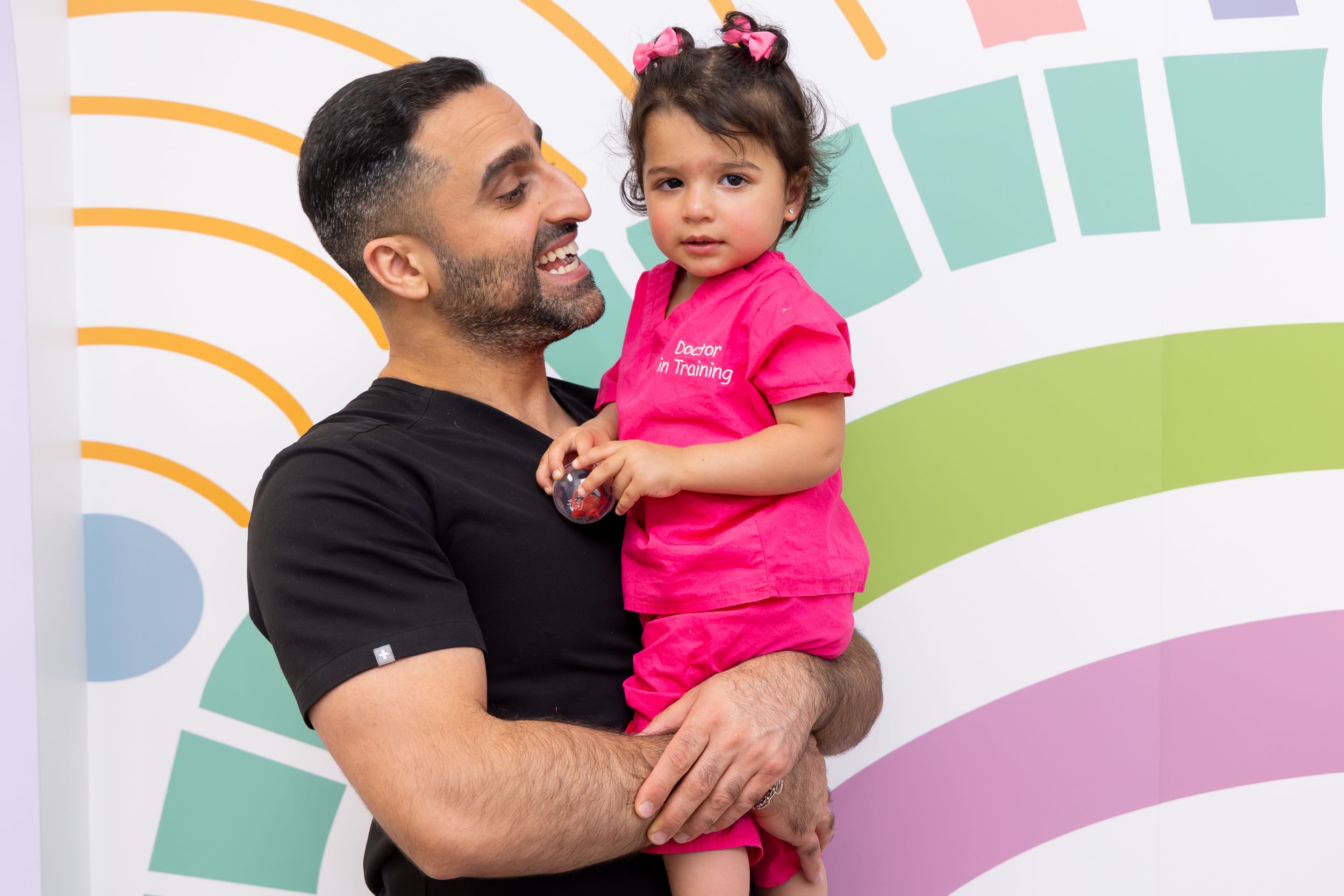 Smiling man holding child in pink outfit.
