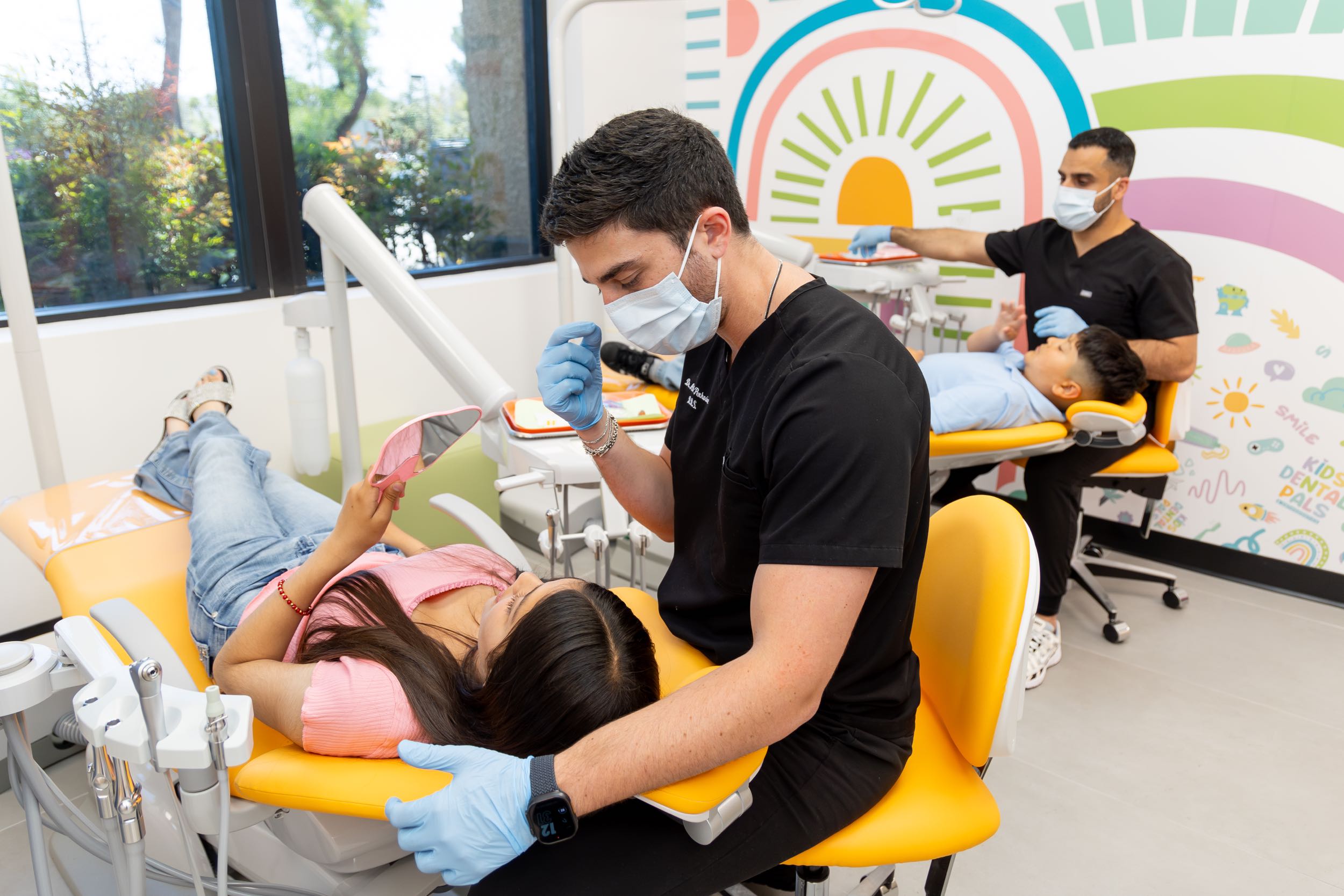Dentists treating young patients in colorful office.