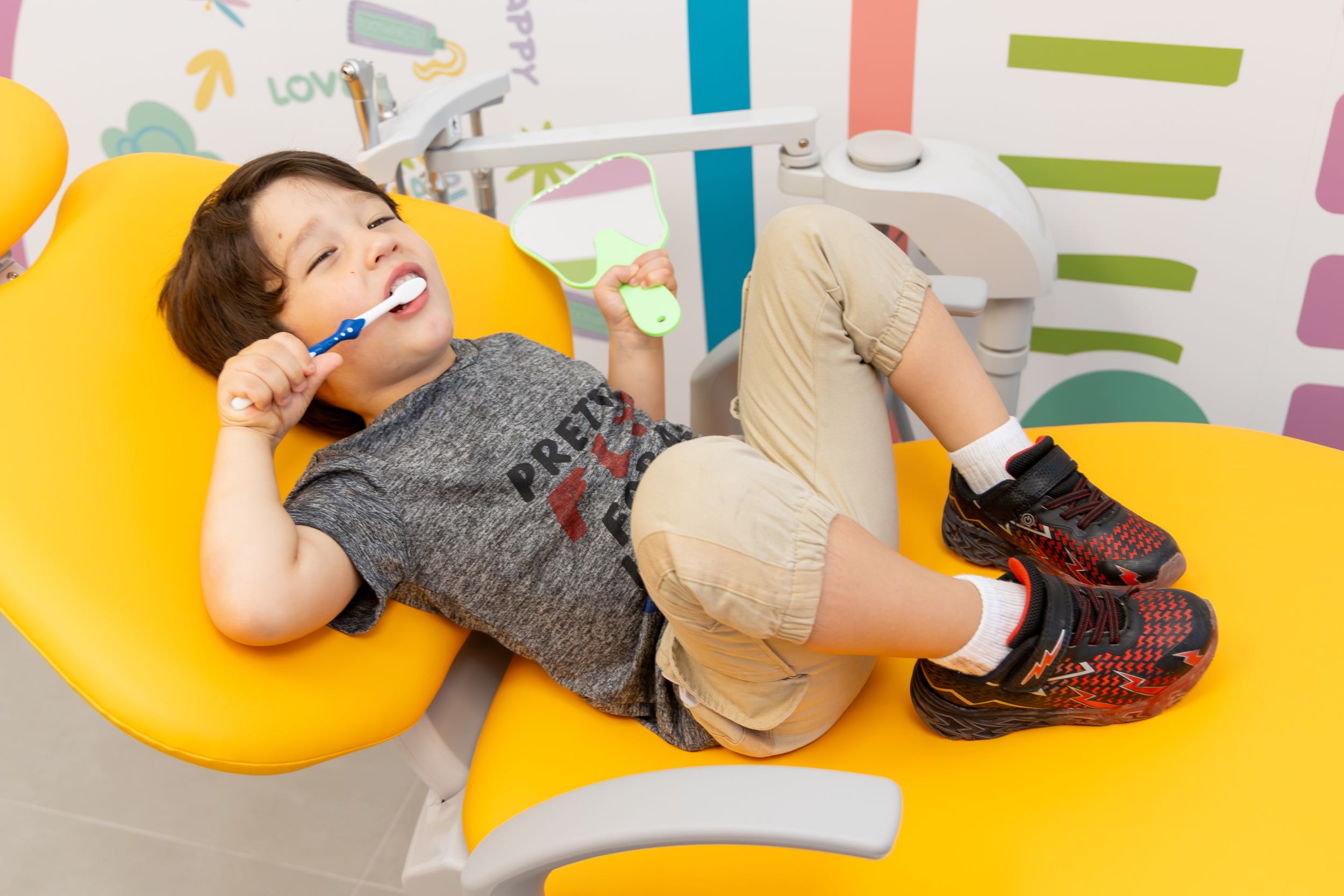 Child brushing teeth in dental chair.