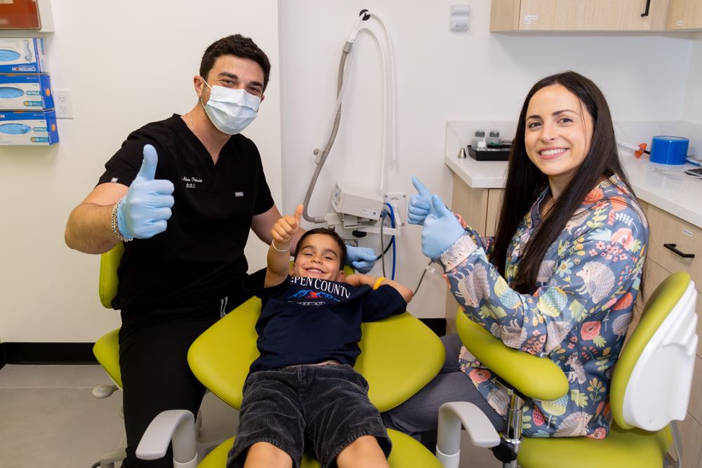 Smiling child at dentist with supportive dental staff.