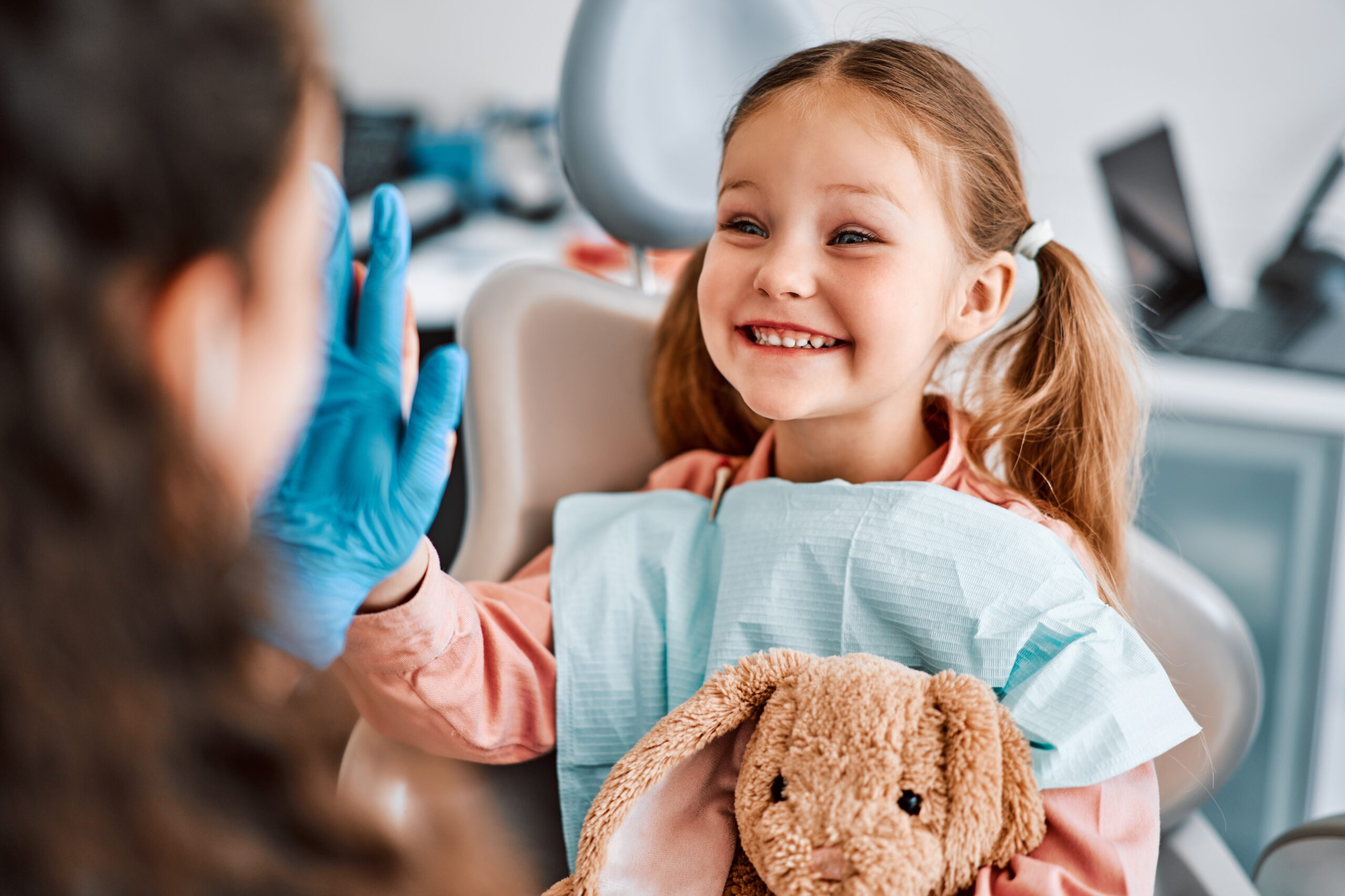 Smiling child high-fives dentist holding stuffed bunny.